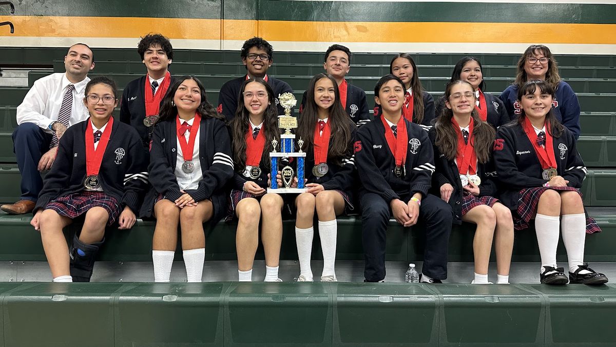 SSFP Academic Decathlon team in uniform with medals and their trophy, seated in the stands with their coaches